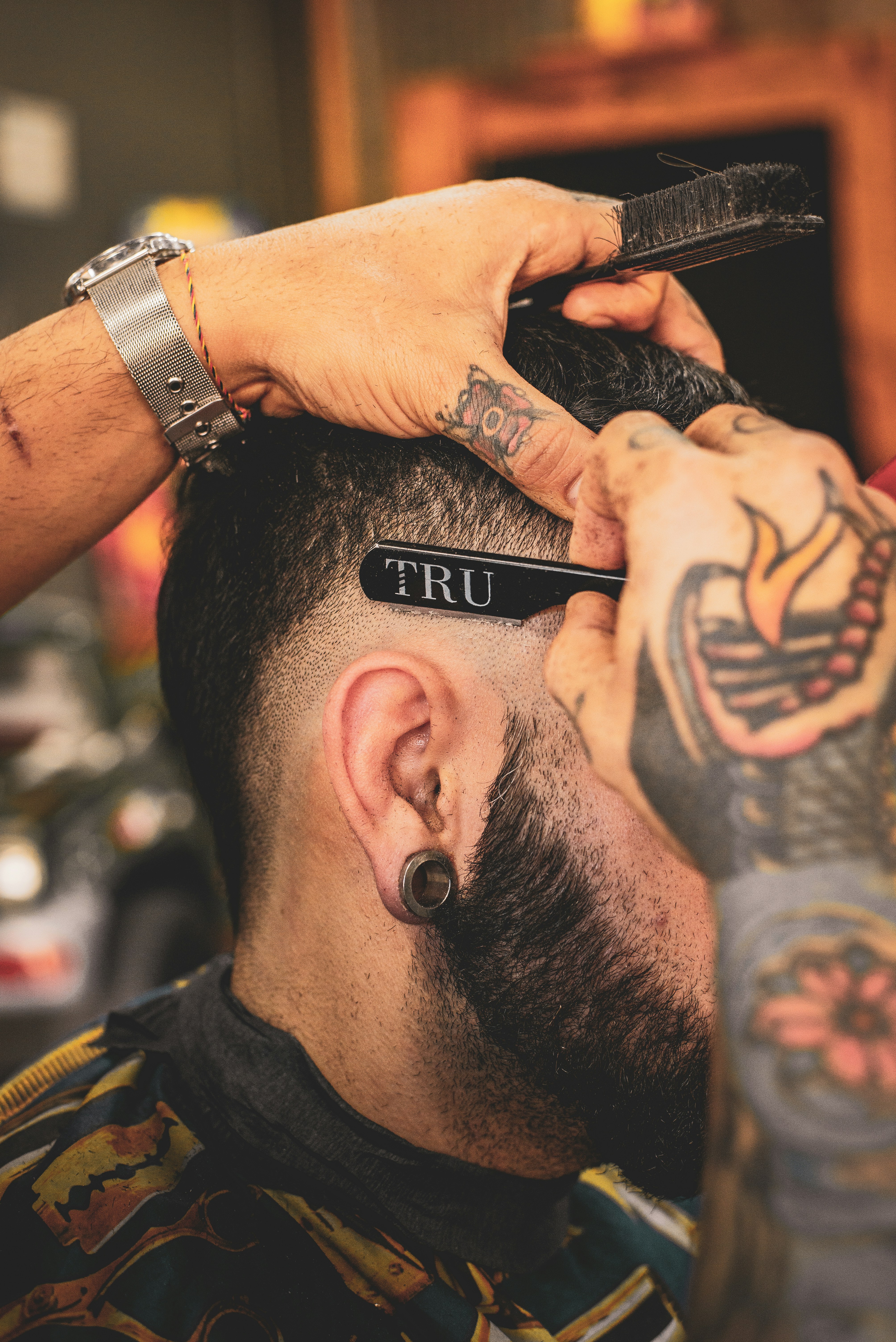 Coiffeur tatoué rasant la nuque d'un client barbu avec